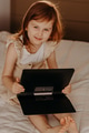 Toddler girl lying on bed in modern room, using laptop tablet pad gadget, looking at camera Toddler girl lying on bed in modern room, using laptop tablet pad gadget, looking at camera - PhotoDune Item for Sale