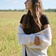 Young woman with long brown hair wrapped in white cardigan stands in sunlit rye field Young woman with long brown hair wrapped in white cardigan stands in sunlit rye field - PhotoDune Item for Sale