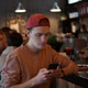 A young man holding a mobile phone while sitting in a cafe A young man holding a mobile phone while sitting in a cafe - PhotoDune Item for Sale
