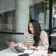 Asian woman smiling and looking at laptop aside book and coffee sitting at table in cafe or building Asian woman smiling and looking at laptop aside book and coffee sitting at table in cafe or building - PhotoDune Item for Sale