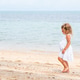 A little girl with curly hair in a white dress walks on a sandy beach. A cute child A little girl with curly hair in a white dress walks on a sandy beach. A cute child - PhotoDune Item for Sale