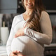 Smiling pregnant woman holding belly in a bright home kitchen Smiling pregnant woman holding belly in a bright home kitchen - PhotoDune Item for Sale