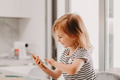 Cute toddler little girl holding smartphone, sitting at table at kitchen, kids using technology Cute toddler little girl holding smartphone, sitting at table at kitchen, kids using technology - PhotoDune Item for Sale