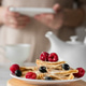 Pancakes with berries for breakfast. Woman holding a mobile phone Pancakes with berries for breakfast. Woman holding a mobile phone - PhotoDune Item for Sale