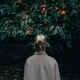 Rear view of woman in a coat stands under a persimmon tree in a quiet garden, autumn mood. Rear view of woman in a coat stands under a persimmon tree in a quiet garden, autumn mood. - PhotoDune Item for Sale