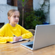 Young girl in yellow sweatshirt studying online at wooden table outdoors Young girl in yellow sweatshirt studying online at wooden table outdoors - PhotoDune Item for Sale