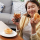 Happy young Asian woman enjoying a sweet glazed donut and iced cola at home. Happy young Asian woman enjoying a sweet glazed donut and iced cola at home. - PhotoDune Item for Sale