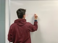College student from behind writing a math formula on a Dry Erase Board while explaining a problem College student from behind writing a math formula on a Dry Erase Board while explaining a problem - PhotoDune Item for Sale