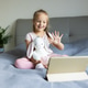Young girl waving at a tablet screen while sitting on a bed with a stuffed animal Young girl waving at a tablet screen while sitting on a bed with a stuffed animal - PhotoDune Item for Sale