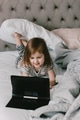 Toddler girl lies in bed, using tablet pad for watching cartoons, resting at home, neutral clors Toddler girl lies in bed, using tablet pad for watching cartoons, resting at home, neutral clors - PhotoDune Item for Sale