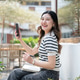 Pretty asian woman holding pen and phone over notebook while sitting on wooden bench in garden cafe. Pretty asian woman holding pen and phone over notebook while sitting on wooden bench in garden cafe. - PhotoDune Item for Sale
