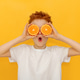 A red-haired boy holds in front of his eyes the halves of a juicy orange on a yellow background A red-haired boy holds in front of his eyes the halves of a juicy orange on a yellow background - PhotoDune Item for Sale