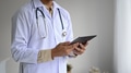 Medical professional in a lab gown with a stethoscope holding a tablet in hand, side view shot. Medical professional in a lab gown with a stethoscope holding a tablet in hand, side view shot. - PhotoDune Item for Sale