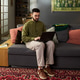 Young Adult Middle Eastern Man Sitting on Sofa Using Laptop in Living Room Young Adult Middle Eastern Man Sitting on Sofa Using Laptop in Living Room - PhotoDune Item for Sale
