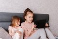 Two little girls sisters sitting in bedroom, holding gadgets. Kids using technologies at home Two little girls sisters sitting in bedroom, holding gadgets. Kids using technologies at home - PhotoDune Item for Sale