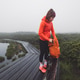 A woman in an orange jacket and beanie stands on a wooden boardwalk near a misty pond, adjusting her A woman in an orange jacket and beanie stands on a wooden boardwalk near a misty pond, adjusting her - PhotoDune Item for Sale