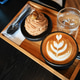 Artistic coffee latte with dessert on a wooden tray in a cozy cafe setting. Artistic coffee latte with dessert on a wooden tray in a cozy cafe setting. - PhotoDune Item for Sale