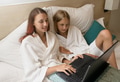 Two sisters in bathrobes are sitting with mugs on the bed in the hotel and watching movie on laptop Two sisters in bathrobes are sitting with mugs on the bed in the hotel and watching movie on laptop - PhotoDune Item for Sale