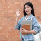 Asian woman student holding laptop over book doing OK hand gesture standing in front of a brick wall Asian woman student holding laptop over book doing OK hand gesture standing in front of a brick wall - PhotoDune Item for Sale