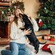 Woman playing with a dog sitting on the floor by the fireplace, on Christmas Eve Woman playing with a dog sitting on the floor by the fireplace, on Christmas Eve - PhotoDune Item for Sale