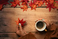 Woman holding a cup of hot coffee and maple leaves on wooden table. Autumn season concept. Woman holding a cup of hot coffee and maple leaves on wooden table. Autumn season concept. - PhotoDune Item for Sale
