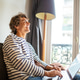 Happy young man sitting on sofa by window with laptop at home Happy young man sitting on sofa by window with laptop at home - PhotoDune Item for Sale