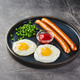 Classic breakfast of fried eggs, sausages and green peas on dish on gray background Classic breakfast of fried eggs, sausages and green peas on dish on gray background - PhotoDune Item for Sale