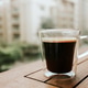 Freshly brewed coffee in a glass cup on a wooden table with a blurred city background Freshly brewed coffee in a glass cup on a wooden table with a blurred city background - PhotoDune Item for Sale