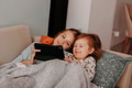 Two sisters lying on couch together at home and using tablet pad for video call. Two sisters lying on couch together at home and using tablet pad for video call. - PhotoDune Item for Sale