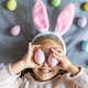 Smiling young girl with bunny ears playing with pastel eggs on a bed Smiling young girl with bunny ears playing with pastel eggs on a bed - PhotoDune Item for Sale
