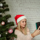 Cute teenage girl in Santa hat making selfie near Christmas tree Cute teenage girl in Santa hat making selfie near Christmas tree - PhotoDune Item for Sale