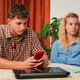 Frustrated young couple sitting at a table, engrossed in their smartphones with visible tension Frustrated young couple sitting at a table, engrossed in their smartphones with visible tension - PhotoDune Item for Sale