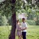 man and a woman in love in a dress and hat stand on a green field under a tree man and a woman in love in a dress and hat stand on a green field under a tree - PhotoDune Item for Sale