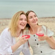 Young girlfriends enjoying pink wine picnic by sea on bright day Young girlfriends enjoying pink wine picnic by sea on bright day - PhotoDune Item for Sale