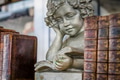 Angelic boy angel statue reading a book between a stack of old books, outside market for sale. Angelic boy angel statue reading a book between a stack of old books, outside market for sale. - PhotoDune Item for Sale