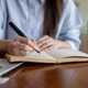Close up of blue shirt woman writing in notebook with a fountain pen sitting at cafe's wooden table Close up of blue shirt woman writing in notebook with a fountain pen sitting at cafe's wooden table - PhotoDune Item for Sale