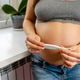 An expectant mother in a serene home setting. She gently holds a thermometer An expectant mother in a serene home setting. She gently holds a thermometer - PhotoDune Item for Sale