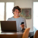 Smiling young man sitting at home working on laptop and using mobile phone Smiling young man sitting at home working on laptop and using mobile phone - PhotoDune Item for Sale