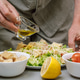 A man cooks in the kitchen. Pours the sauce over the ready-made delicious Caesar salad. Close-up. A man cooks in the kitchen. Pours the sauce over the ready-made delicious Caesar salad. Close-up. - PhotoDune Item for Sale