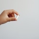 A close-up of a hand holding a white capsule against a light background A close-up of a hand holding a white capsule against a light background - PhotoDune Item for Sale