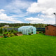 Backyard greenhouse made of foil standing on the grass behind the house. Backyard greenhouse made of foil standing on the grass behind the house. - PhotoDune Item for Sale