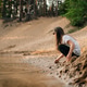 Curious girl with brown hair squatting down on sand near river in forest and going to take grit Curious girl with brown hair squatting down on sand near river in forest and going to take grit - PhotoDune Item for Sale