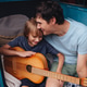 Happy family. Father with son sitting in camping trailer and boy play the guitar Dad hugs the son Happy family. Father with son sitting in camping trailer and boy play the guitar Dad hugs the son - PhotoDune Item for Sale