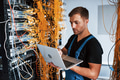 Young man in uniform and with laptop works with internet equipment and wires in server room Young man in uniform and with laptop works with internet equipment and wires in server room - PhotoDune Item for Sale