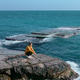 a woman sits on a stone near the sea, blue beautiful background a woman sits on a stone near the sea, blue beautiful background - PhotoDune Item for Sale