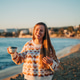 Young beautiful girl in cozy sweater holding coffee cup and smiling into the camera on seaside shore Young beautiful girl in cozy sweater holding coffee cup and smiling into the camera on seaside shore - PhotoDune Item for Sale