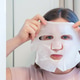 Young woman applying cloth sheet mask on her face front view. Young woman applying cloth sheet mask on her face front view. - PhotoDune Item for Sale