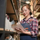 Woman in apron checking inventory on clipboard in a warehouse setting Woman in apron checking inventory on clipboard in a warehouse setting - PhotoDune Item for Sale
