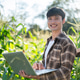 Happy asian farmer man in checkered shirt holding laptop while standing in corp farm under sunlight. Happy asian farmer man in checkered shirt holding laptop while standing in corp farm under sunlight. - PhotoDune Item for Sale