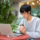 Glasses asian man holding coffee both hands looking at laptop while sitting at table in garden cafe. Glasses asian man holding coffee both hands looking at laptop while sitting at table in garden cafe. - PhotoDune Item for Sale
